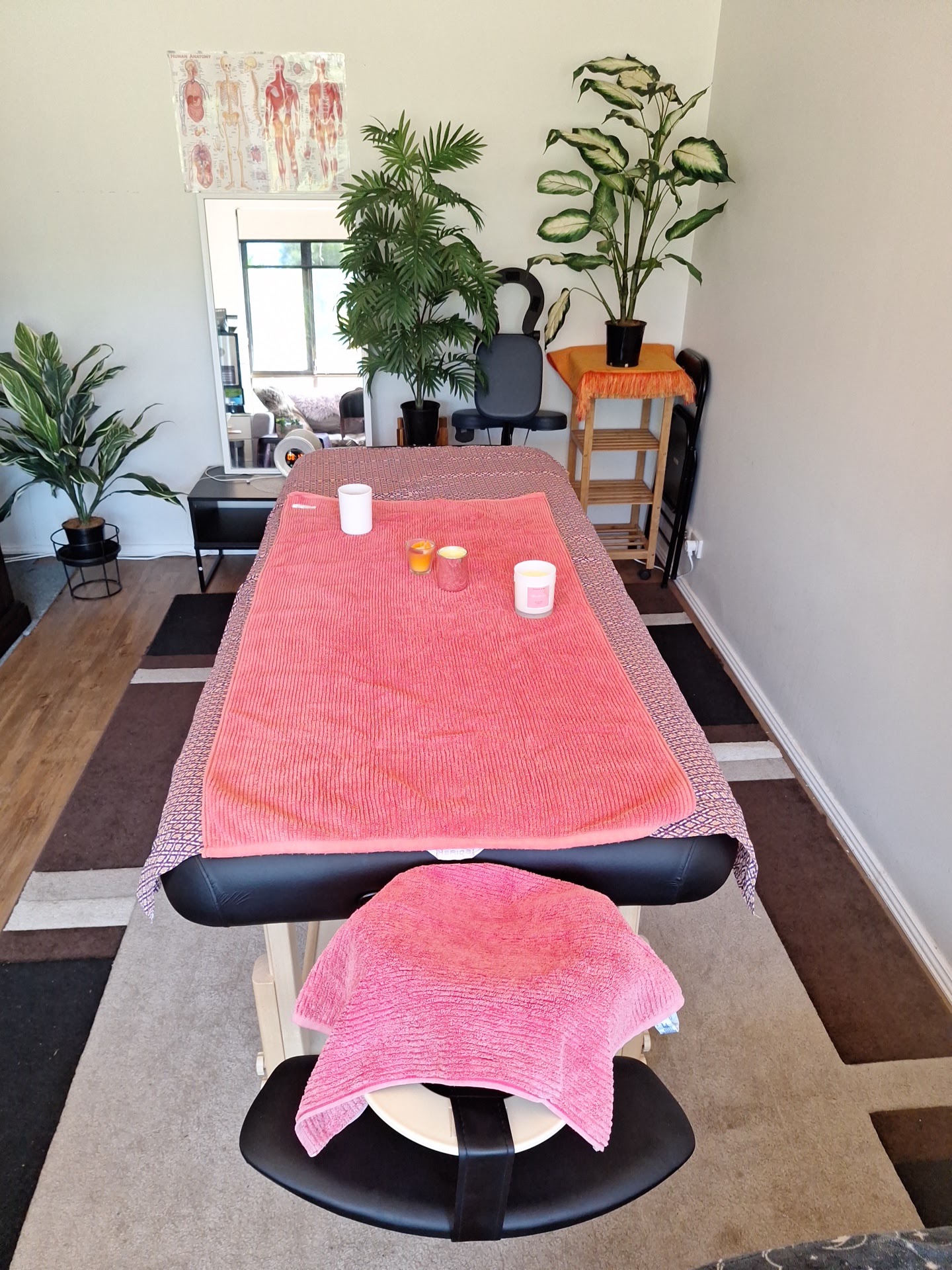 Neena's treatment room in Safety Bay: massage table dressed in coral towels, candles, and indoor plants