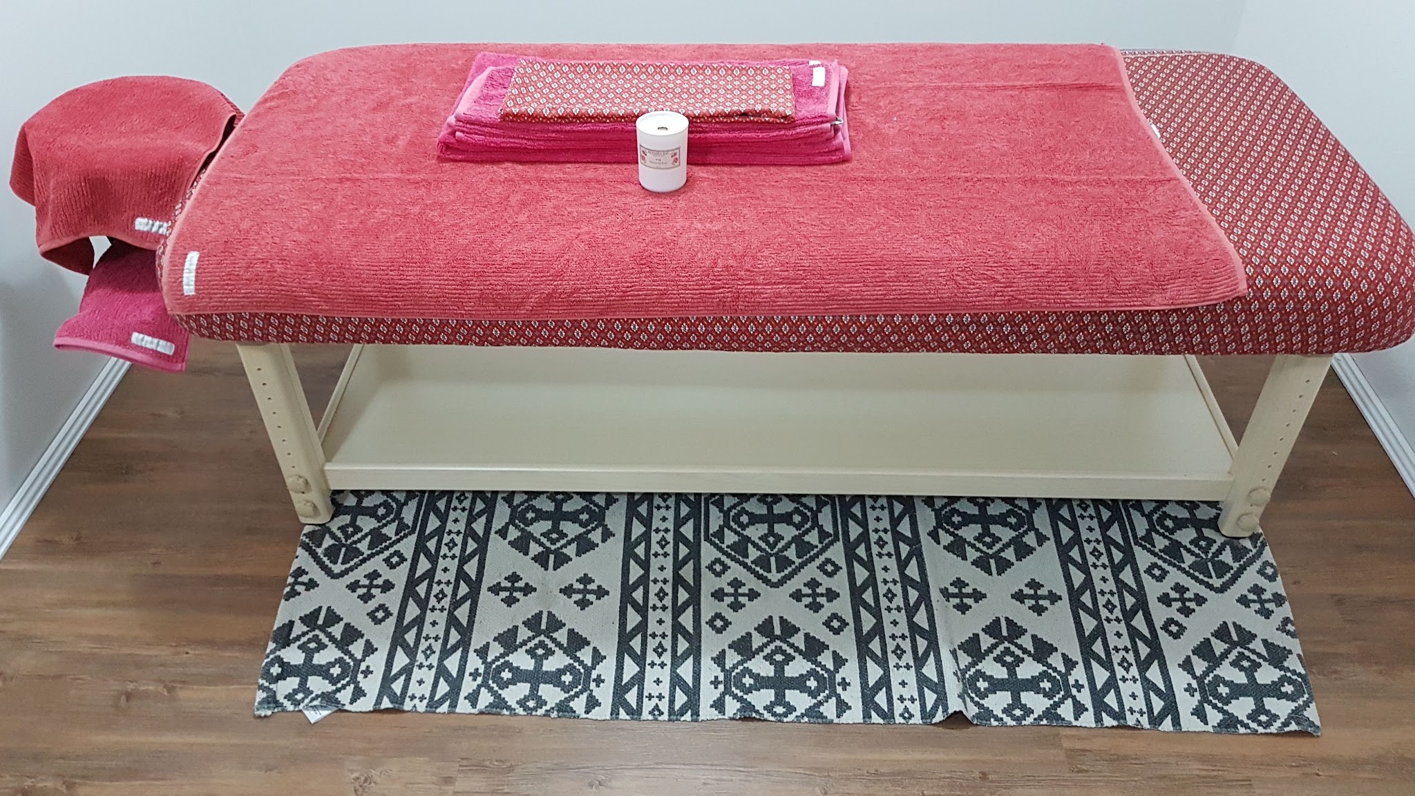 Massage table set with coral towels and a candle over a black and white patterned rug
